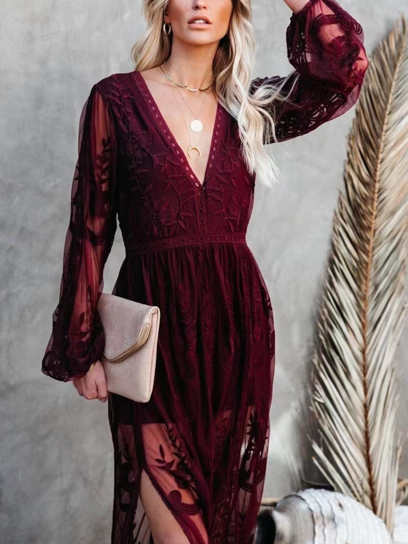NEWYORKLISTED STYLE COLLECTION: Woman wearing a burgundy lace dress with long sleeves, holding a beige clutch against a neutral background.
