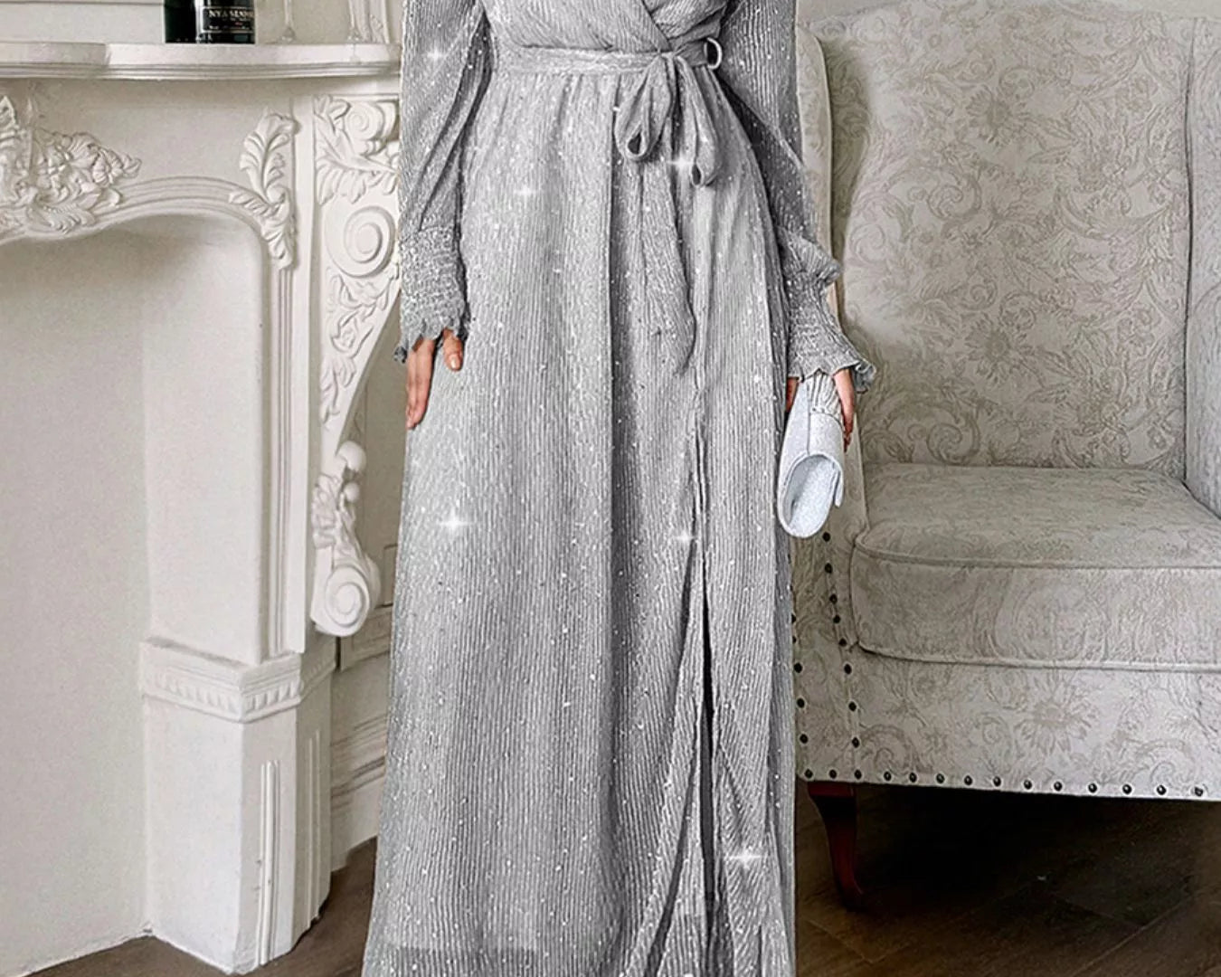 NEWYORKLISTED STYLE COLLECTION: Woman wearing a sparkly gray dress in a room with a fireplace and chair.