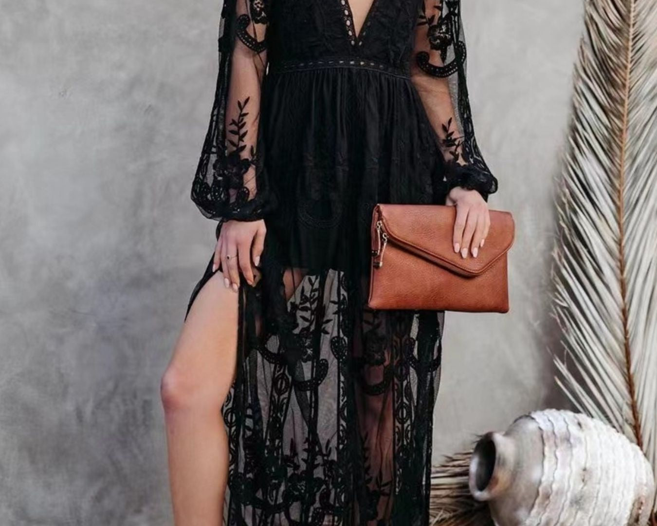 NEWYORKLISTED STYLE COLLECTION: Woman wearing a black lace dress with a slit, holding a brown clutch against a neutral background.