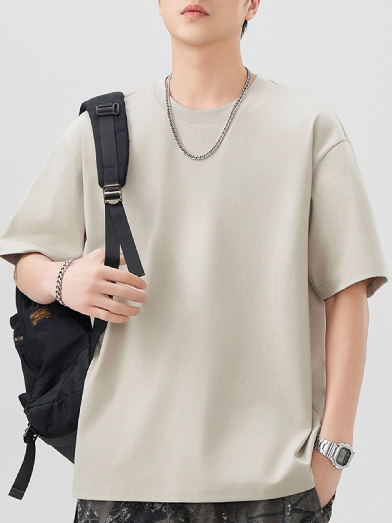 NEWYORKLISTED ATLAS MEN"S COLLECTION: Person wearing a beige t-shirt holding a black backpack against a white background