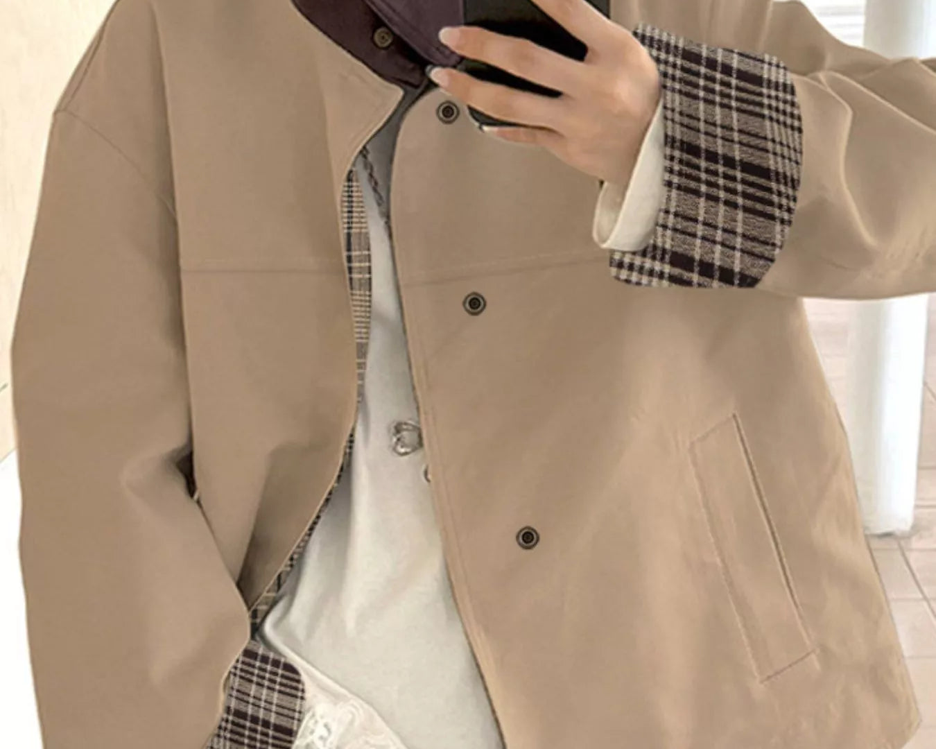 NEWYORKLISTED STYLE COLLECTION Person wearing a beige jacket over a plaid shirt with lace trim, holding a phone.