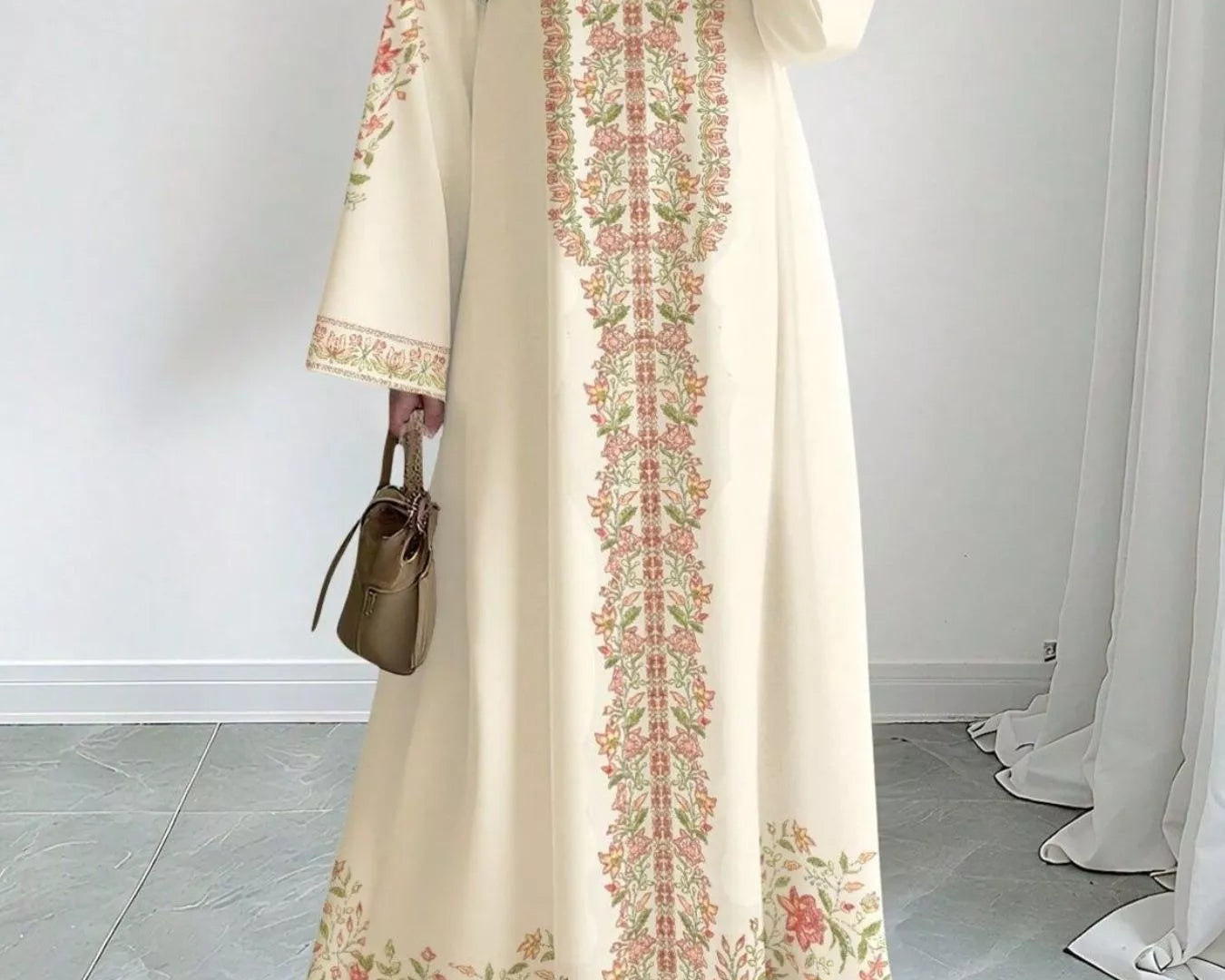 NEWYORKLISTED STYLE COLLECTION: Woman wearing a long, cream-colored dress with floral embroidery in a room with white walls and gray floor.