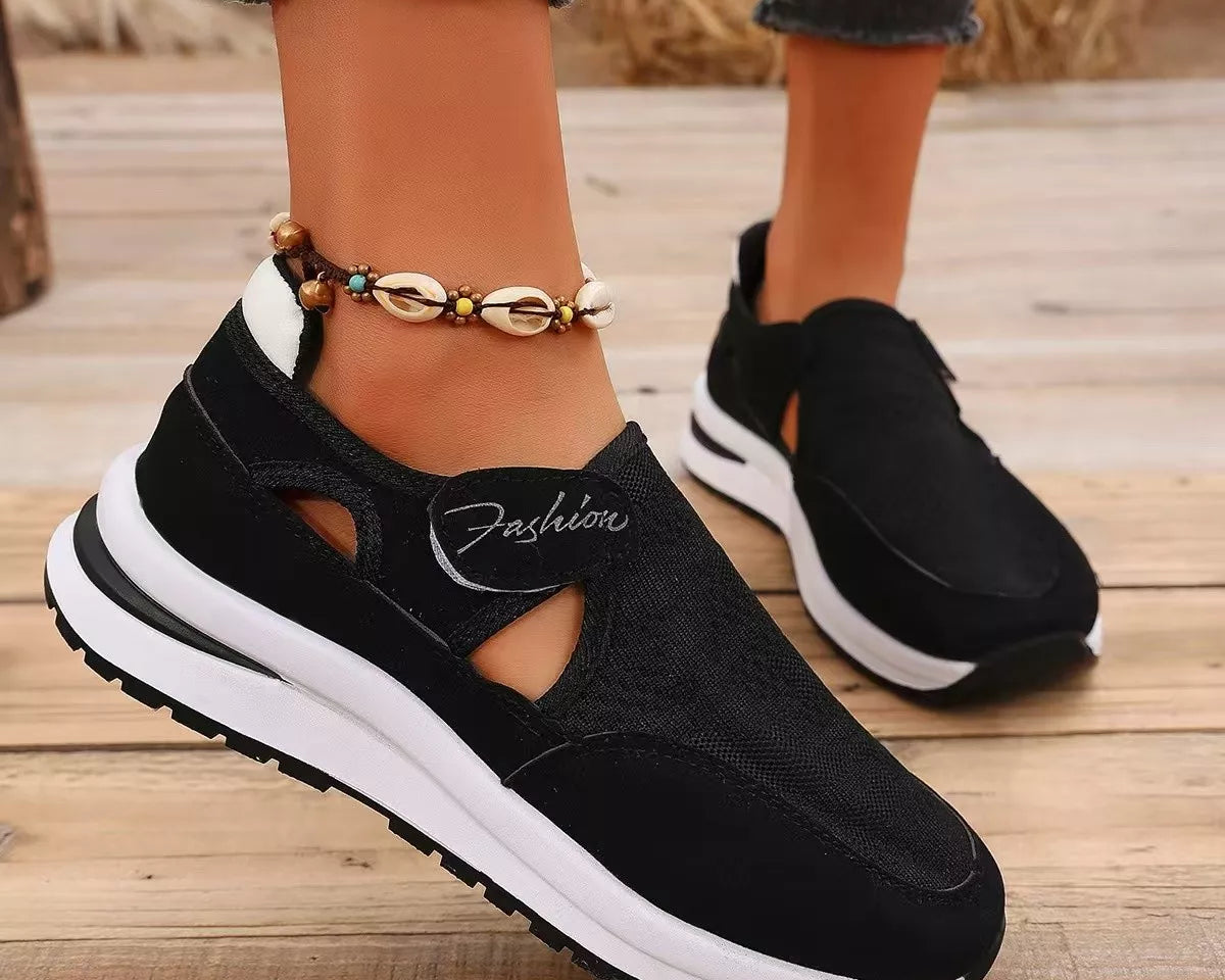 NEWYORKLISTED SHOE COLLECTION: Black slip-on sneakers with white soles worn on a wooden floor.