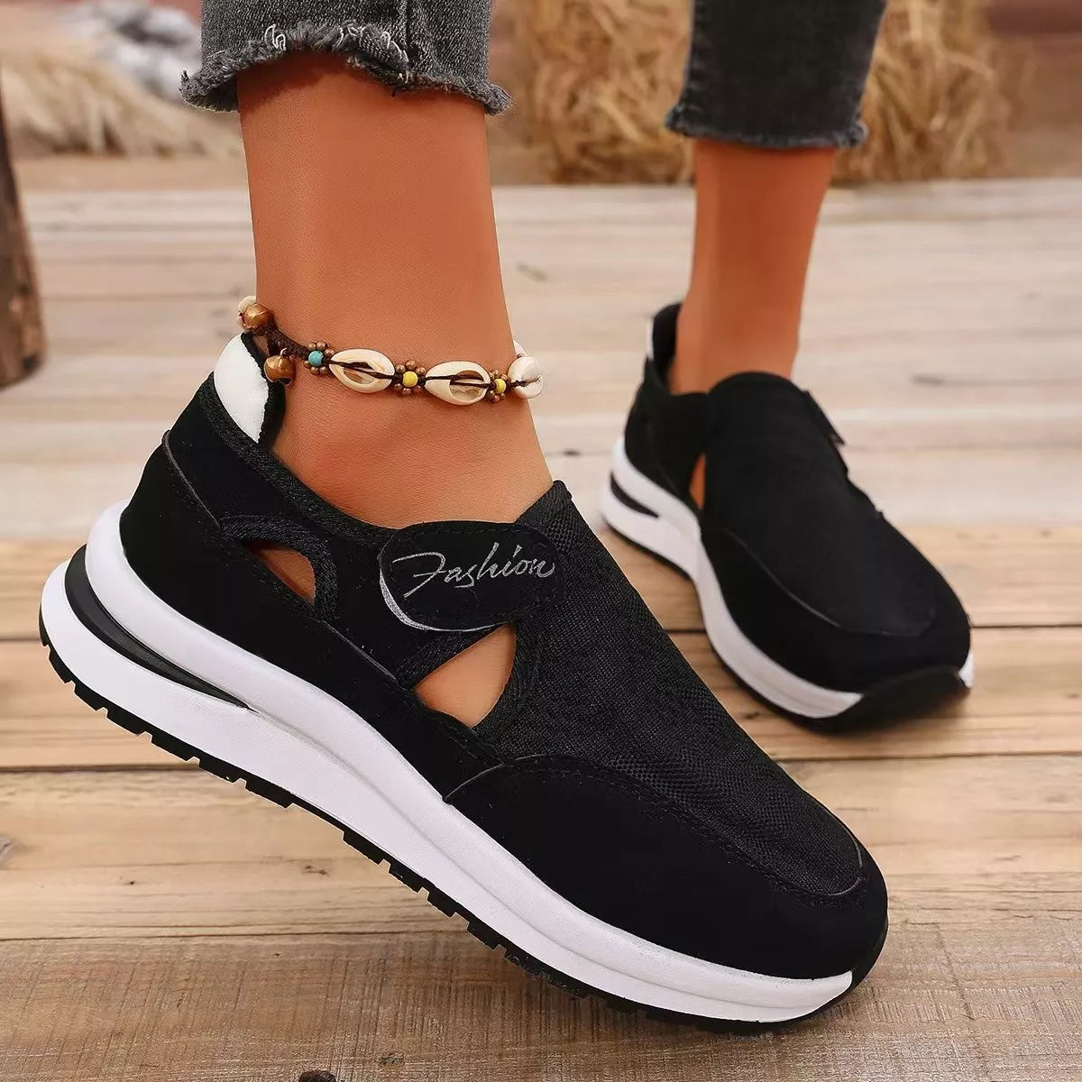 NEWYORKLISTED SHOE COLLECTION: Black slip-on sneakers with white soles worn on a wooden floor.