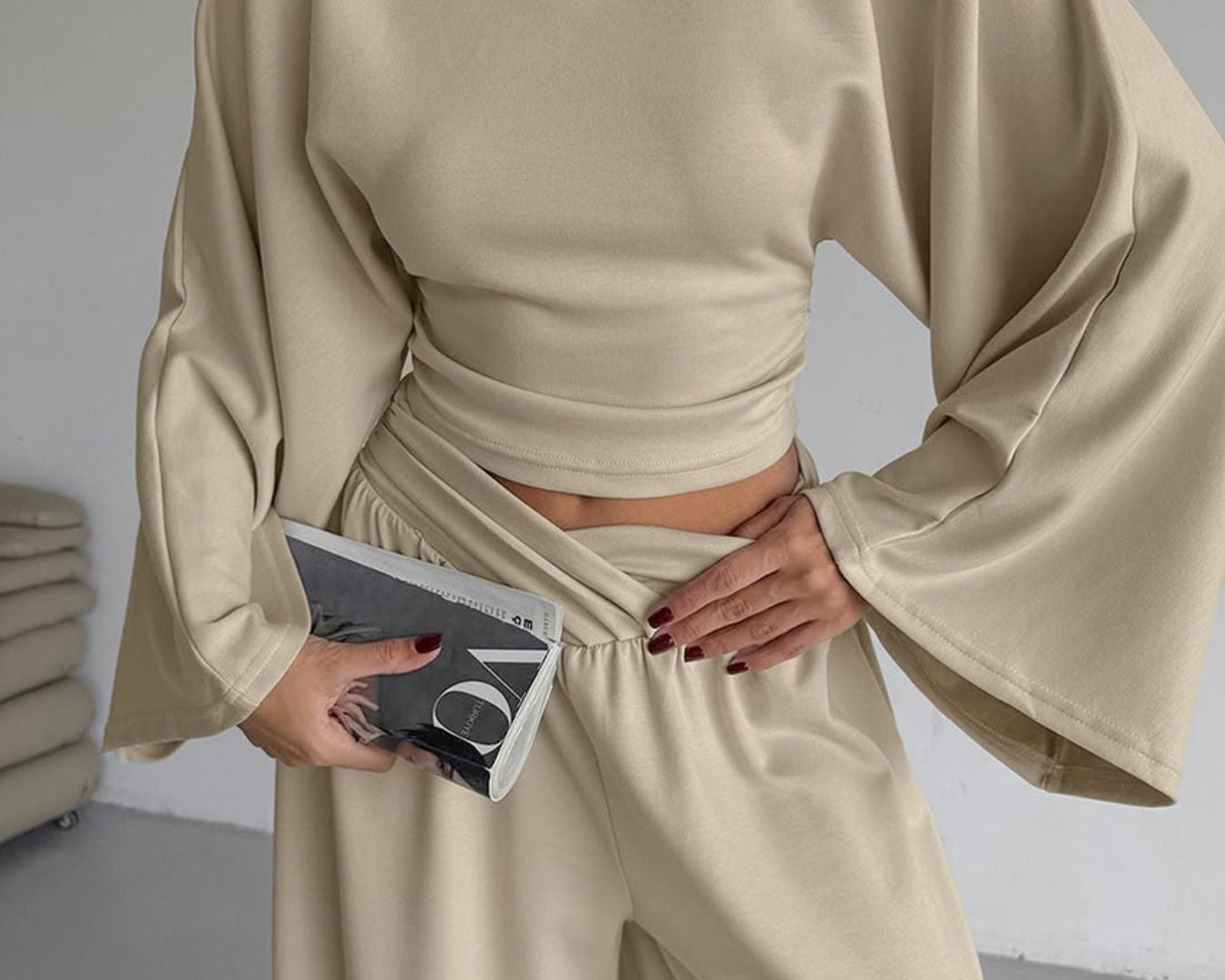 NEWYORKLISTED STYLE COLLECTION: Person wearing a beige outfit holding a phone in a minimal indoor setting