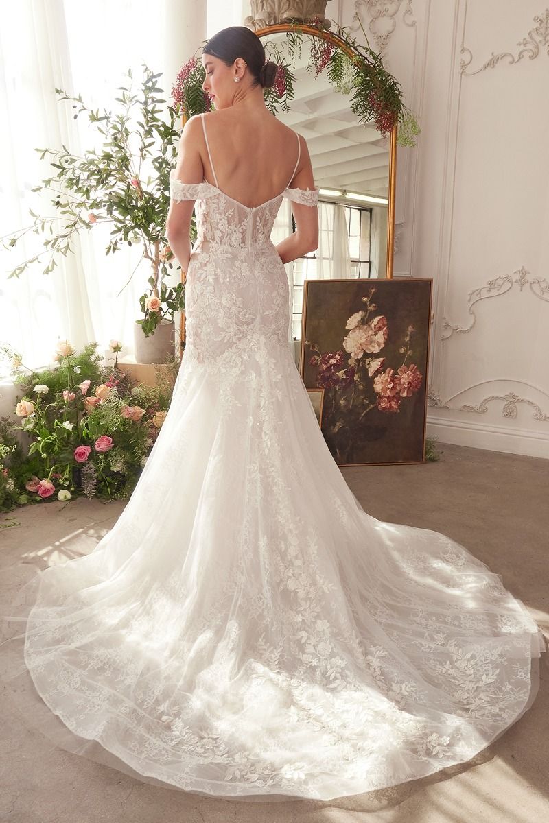 NEWYORKLISTED ELEGANT BRIDE COLLECTION: Woman in a white lace wedding dress standing in a decorated room with flowers and a mirror.