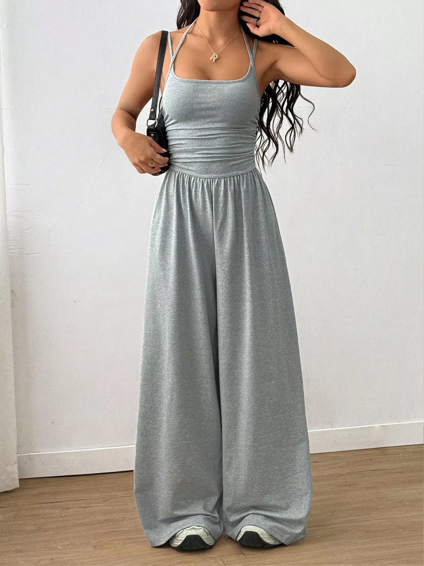 NEWYORKLISTED Comfort Collection: Woman wearing a gray jumpsuit against a white wall.