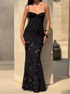 NEWYORKLISTED STYLE COLLECTION: Woman wearing a black evening gown with floral embroidery against a stone wall.