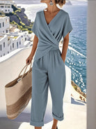 NEWYORKLISTED STYLE COLLECTION: Person wearing a light blue jumpsuit with a scenic background of water and buildings.