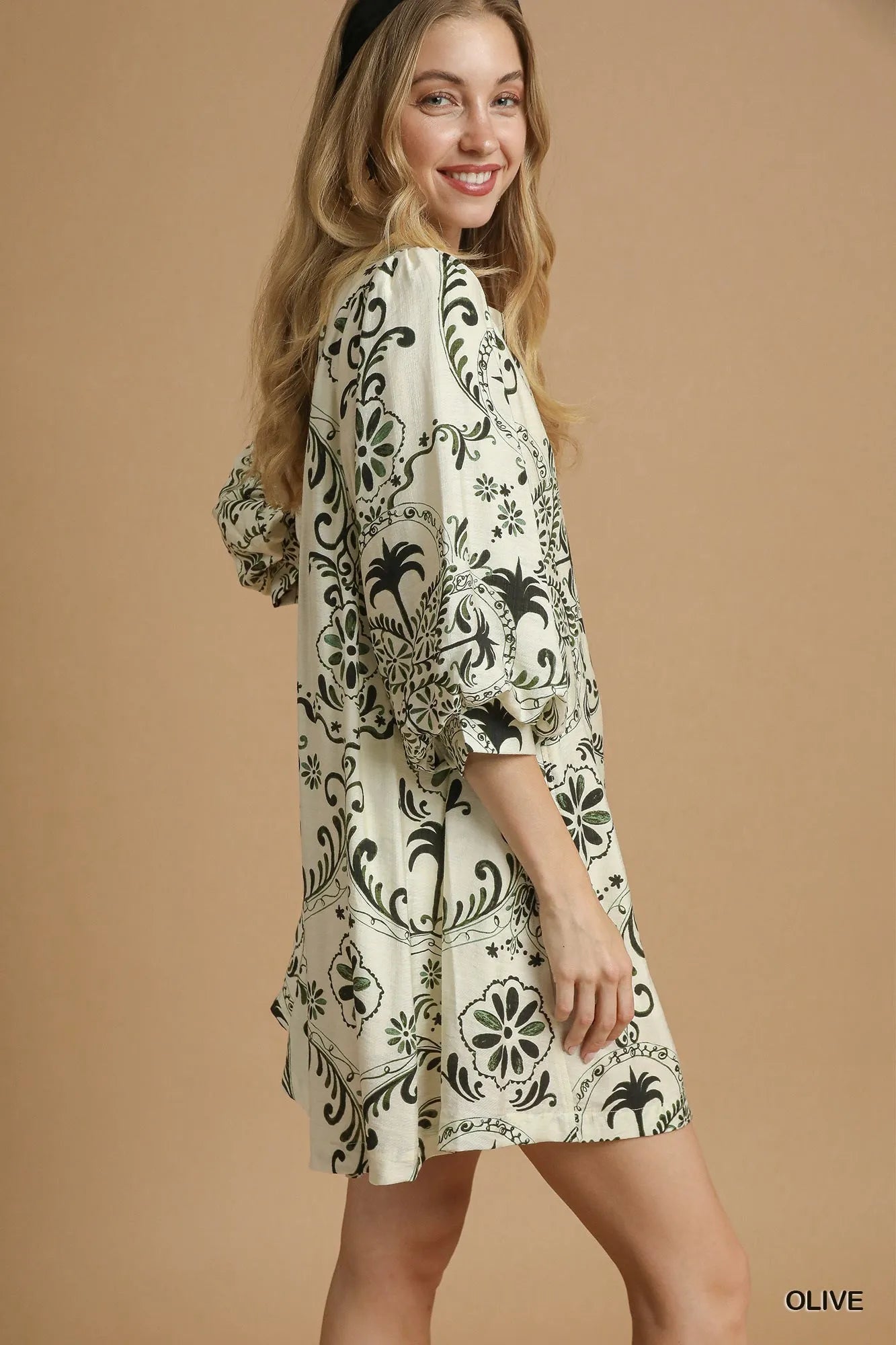 NEWYORKLISTED STYLE COLLECTION: Woman wearing a patterned dress on a beige background