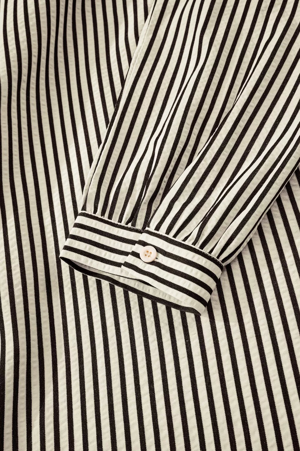 NEWYORKLISTED STYLE COLLECTION: Close-up of a black and white striped shirt with a button detail.