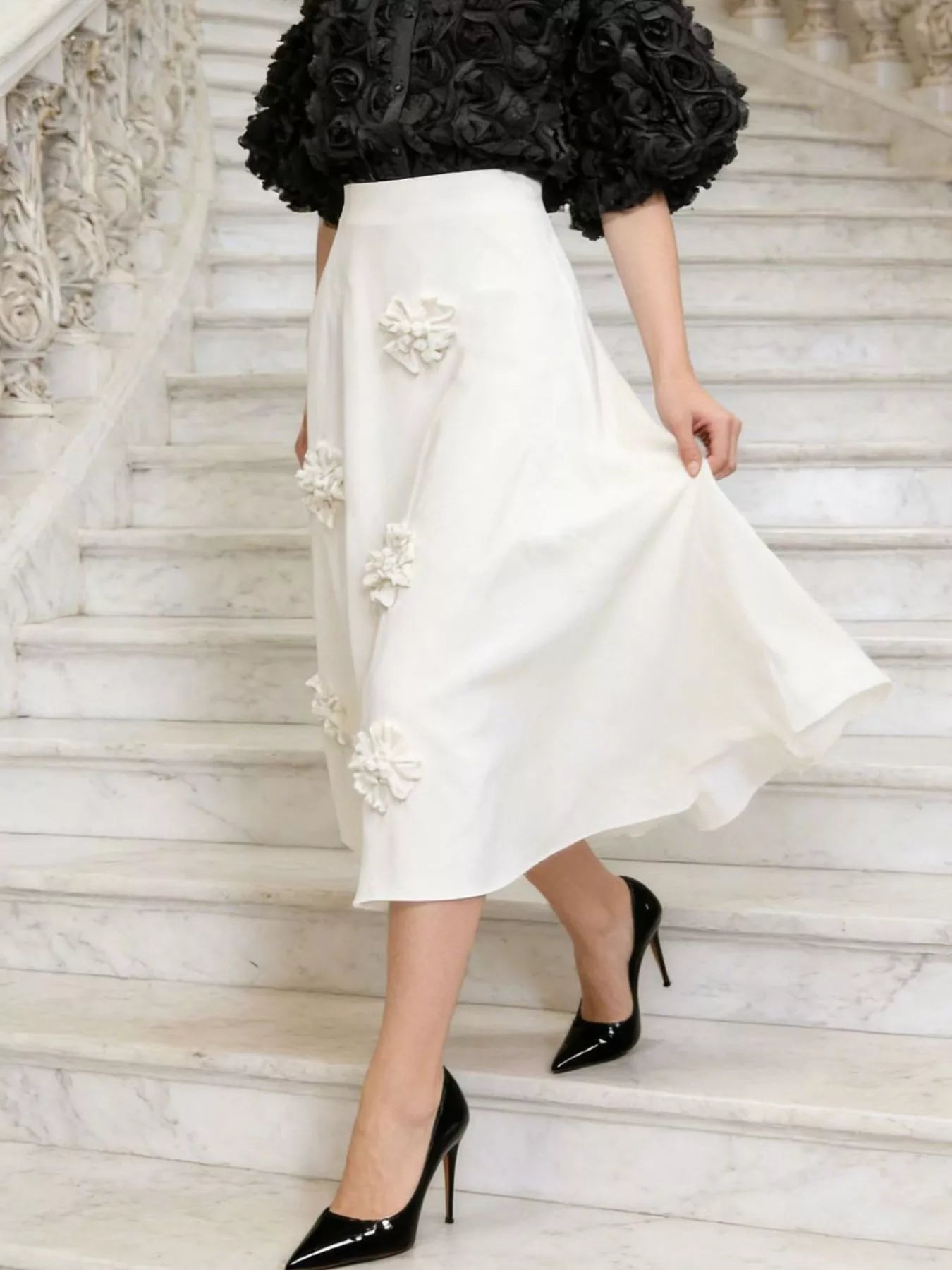 NEWYORKLISTED STYLE COLLECTION: Person wearing a white skirt with floral embellishments on marble stairs