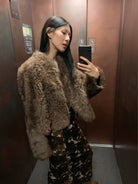NEWYORKLISTED STYLE COLLECTION: Person wearing a fluffy brown coat taking a mirror selfie in an elevator.