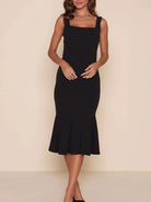 NEWYORKLISTED STYLE COLLECTION: A woman modeling a sleeveless black midi dress with a square neckline, wide shoulder straps, and a flared ruffled hem against a plain beige studio background.