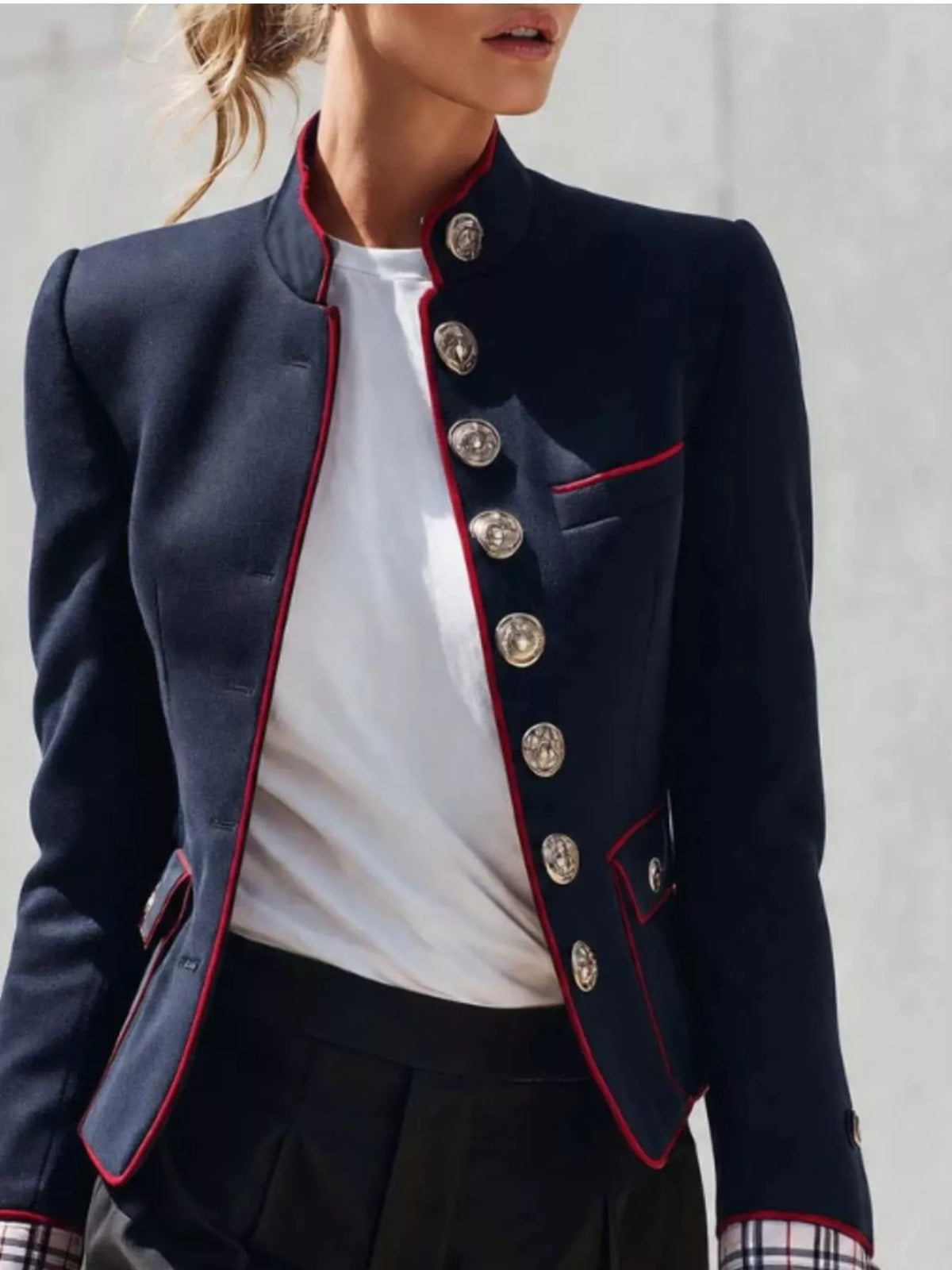 NEWYORKLISTED STYLE COLLECTION:  A cropped navy blue military-style blazer with red piping and large silver buttons, worn by a model over a white top and dark skirt.