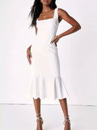 NEWYORKLISTED STYLE COLLECTION: A woman modeling a white sleeveless midi dress with a square neckline, side cutout, and flared ruffle hem against a plain white studio background.