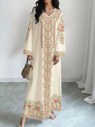 NEWYORKLISTED STYLE COLLECTION: Woman wearing a long, cream-colored dress with floral embroidery in a room with light gray flooring and white walls.