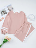 NEWYORKLISTED Comfort Collection: Pink sweatshirt and pants set on a white surface with flowers and photos.