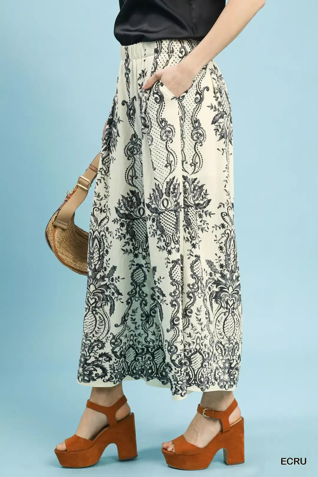 NEWYORKLISTED STYLE COLLECTION: Person wearing a patterned skirt with brown shoes and a bag on a light blue background