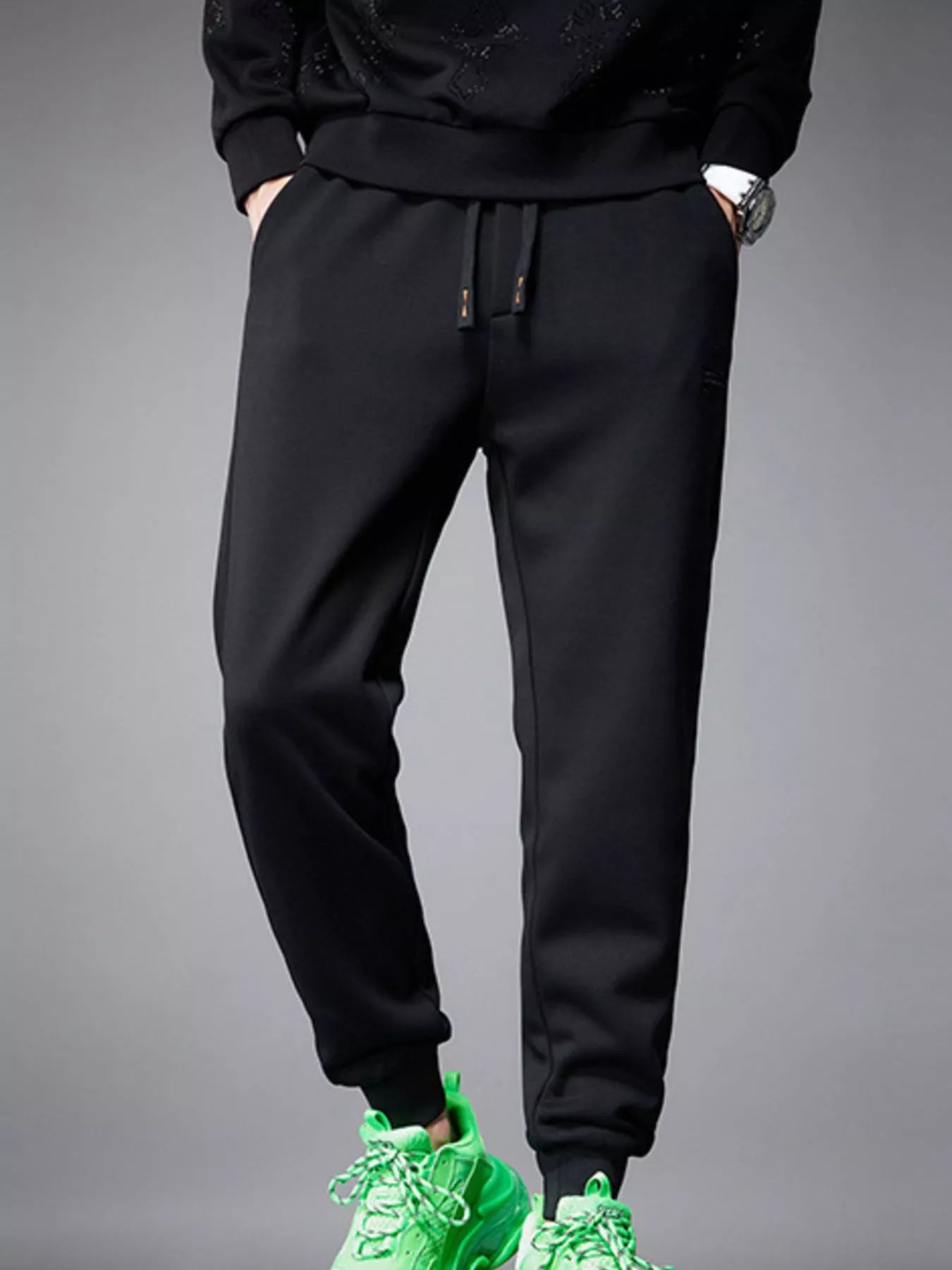 NEWYORKLISTED ATLAS MEN's COLLECTION: Person wearing black jogger pants with green sneakers on a gray background