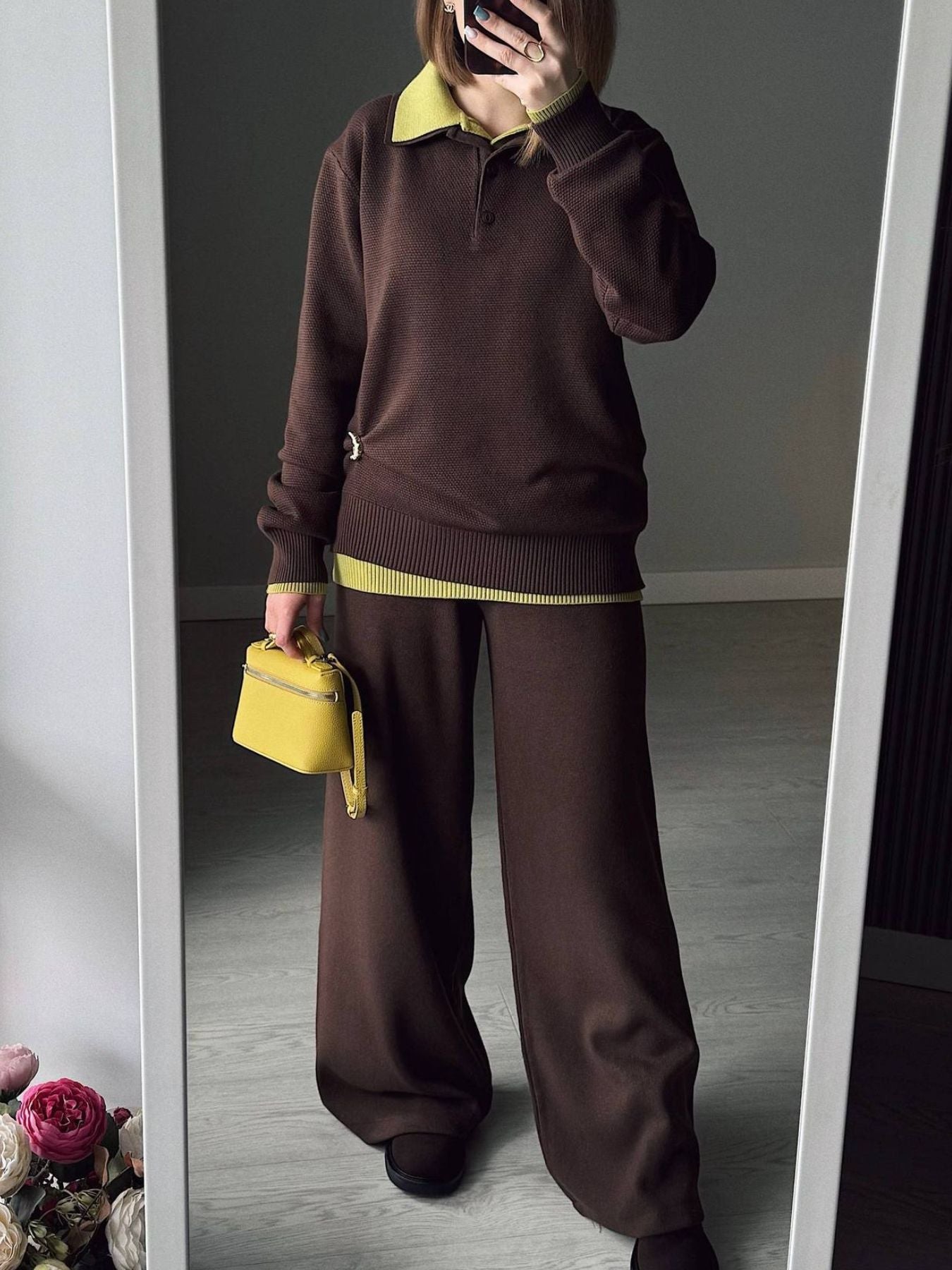 NEWYORKLISTED Comfort Collection: Person wearing a brown outfit with yellow accents, holding a yellow handbag in front of a mirror.