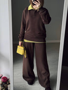 NEWYORKLISTED Comfort Collection: Person wearing a brown outfit with yellow accents, holding a yellow handbag in front of a mirror.