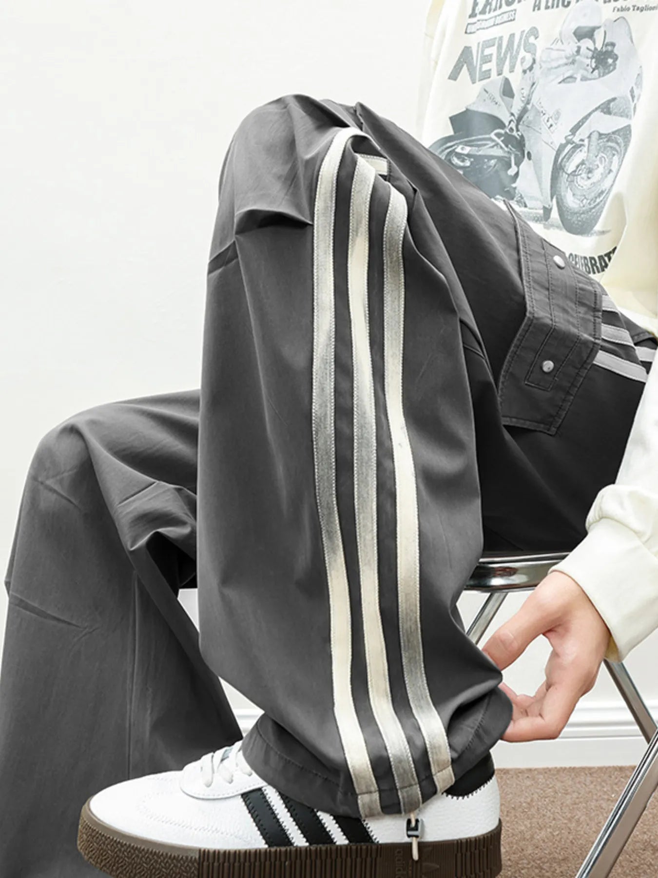 NEWYORKLISTED ATLAS MEN's COLLECTION: Person wearing a dark gray tracksuit with white stripes sitting on a chair.