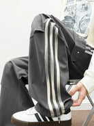 NEWYORKLISTED ATLAS MEN's COLLECTION: Person wearing a dark gray tracksuit with white stripes sitting on a chair.