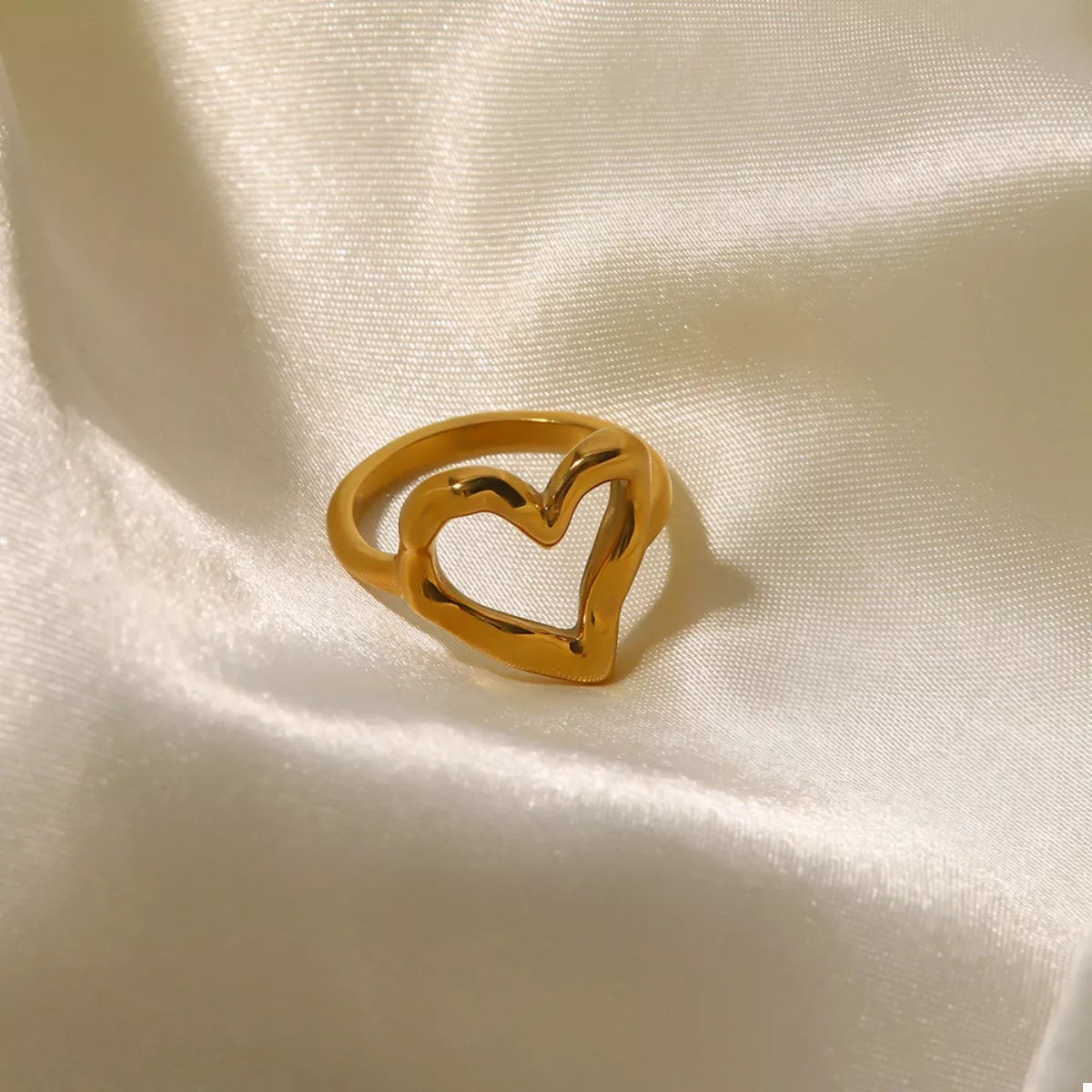 NYLD Glamour Collection by NEWYORKLISTED: Gold heart-shaped ring on a beige fabric background