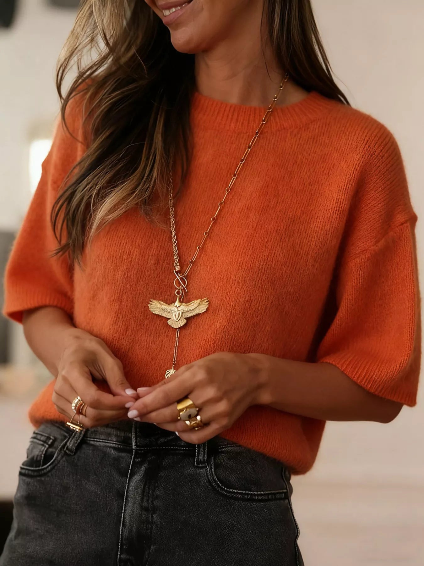 NEWYORKLISTED Style Collection: Person wearing an orange sweater and black pants with a gold necklace and rings.