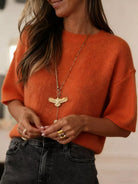 NEWYORKLISTED Style Collection: Person wearing an orange sweater and black pants with a gold necklace and rings.