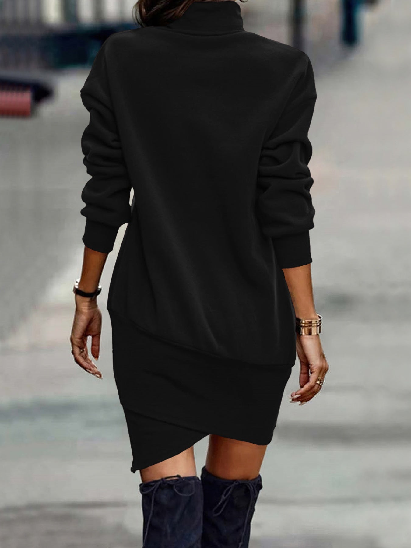 NEWYORKLISTED Style Collection: Person wearing a black dress with long sleeves and an asymmetrical hem, standing on a blurred street background.