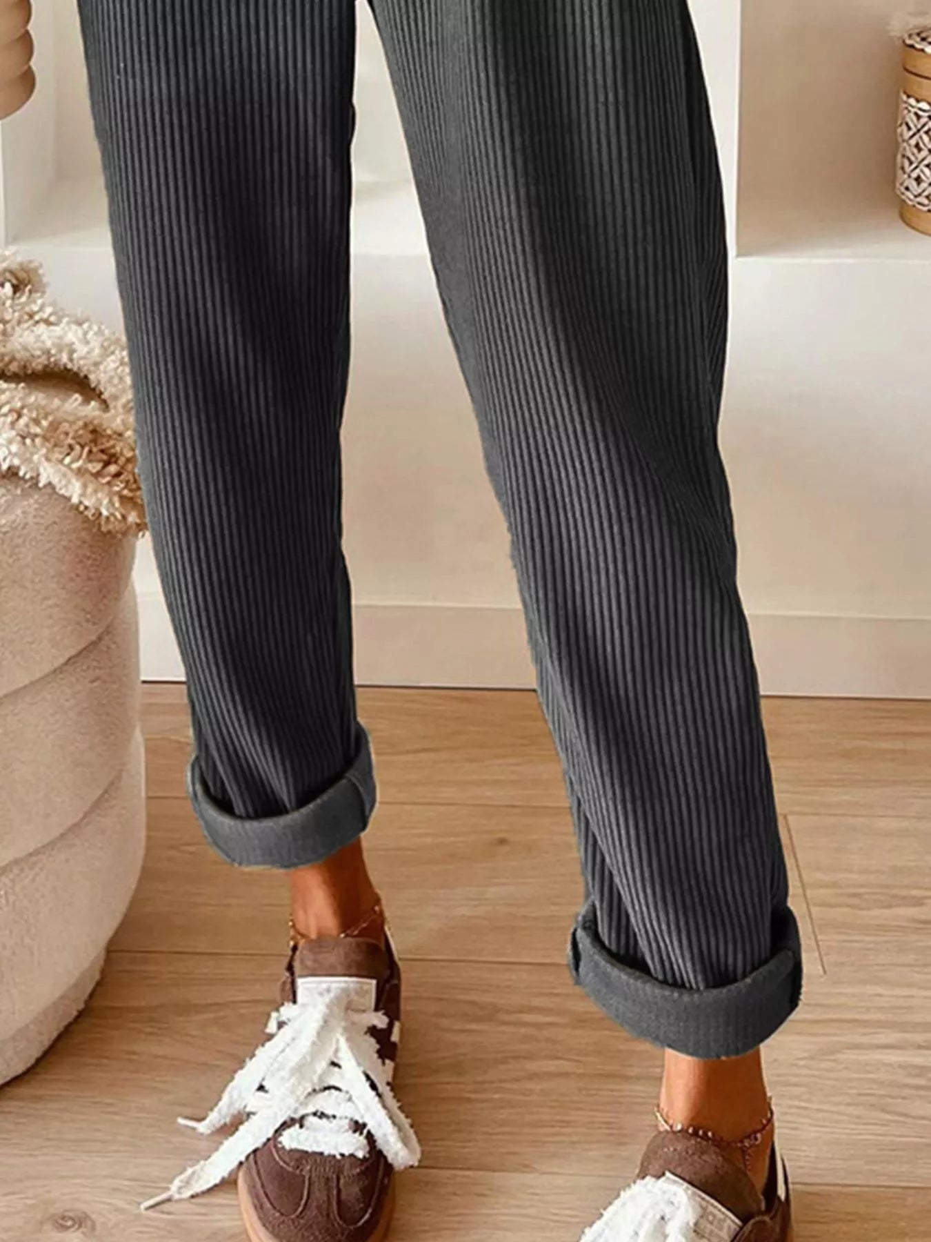 Person wearing dark gray ribbed pants with rolled-up cuffs, standing on a wooden floor.
