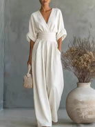 NEWYORKLISTED STYLE COLLECTION: Woman in a white dress standing next to a vase with dried flowers against a gray wall.