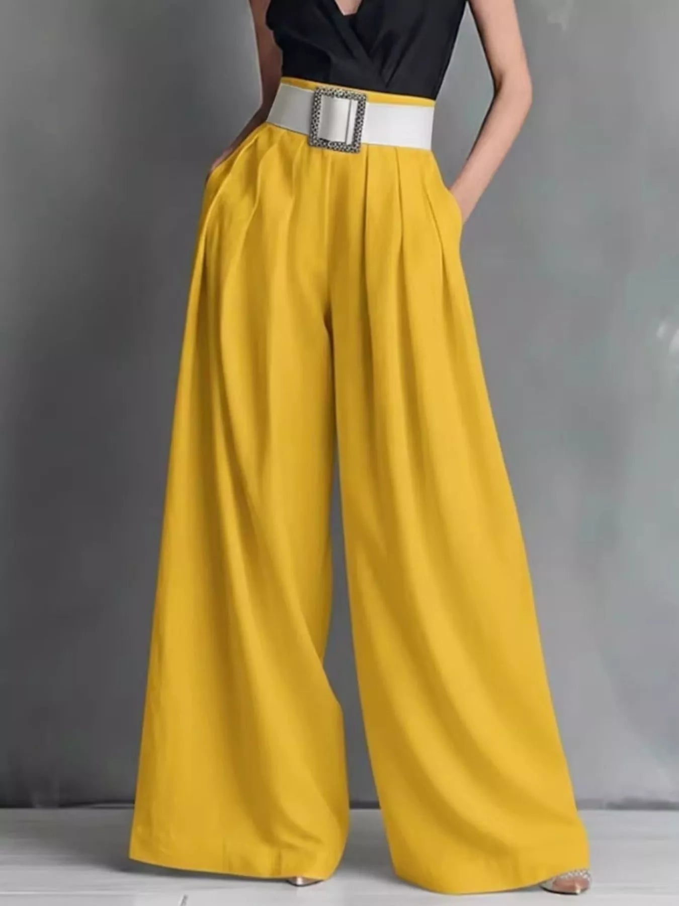 Mustard yellow wide-leg pants with a black top and white belt on a gray background