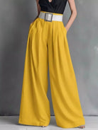 Mustard yellow wide-leg pants with a black top and white belt on a gray background