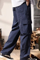 NEWYORKLISTED ATLAS MEN's COLLECTION: Person wearing navy cargo pants in an indoor setting with wooden logs in the background