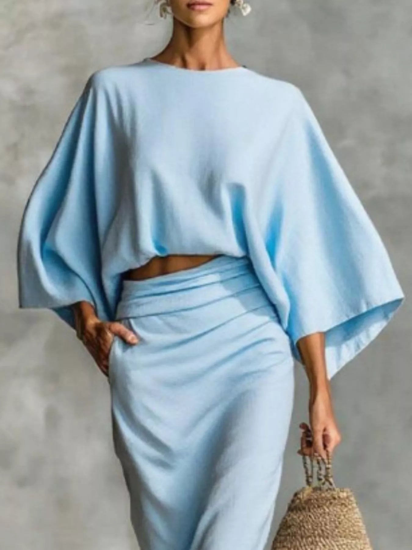 NEWYORKLISTED STYLE COLLECTION: Woman wearing a light blue outfit with a cape-like top against a gray background