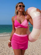 NEWYORKLISTED EDEN COLLECTION: Woman in a pink bikini holding a pink inflatable ring on a beach.