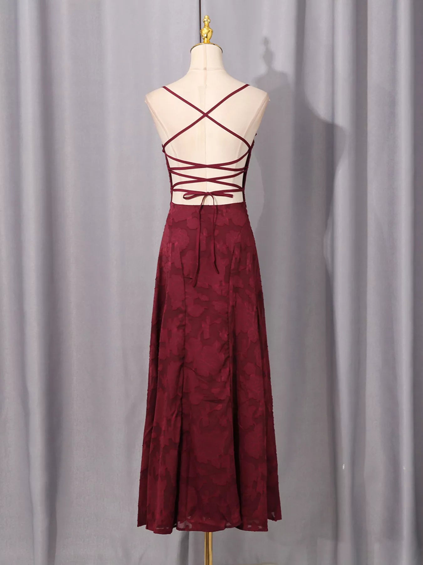 NEWYORKLISTED STYLE COLLECTION: Burgundy dress with criss-cross straps on a mannequin against a gray curtain background