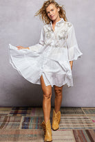 NEWYORKLISTED STYLE COLLECTION: Woman wearing a white embroidered dress with yellow cowboy boots on a textured floor.