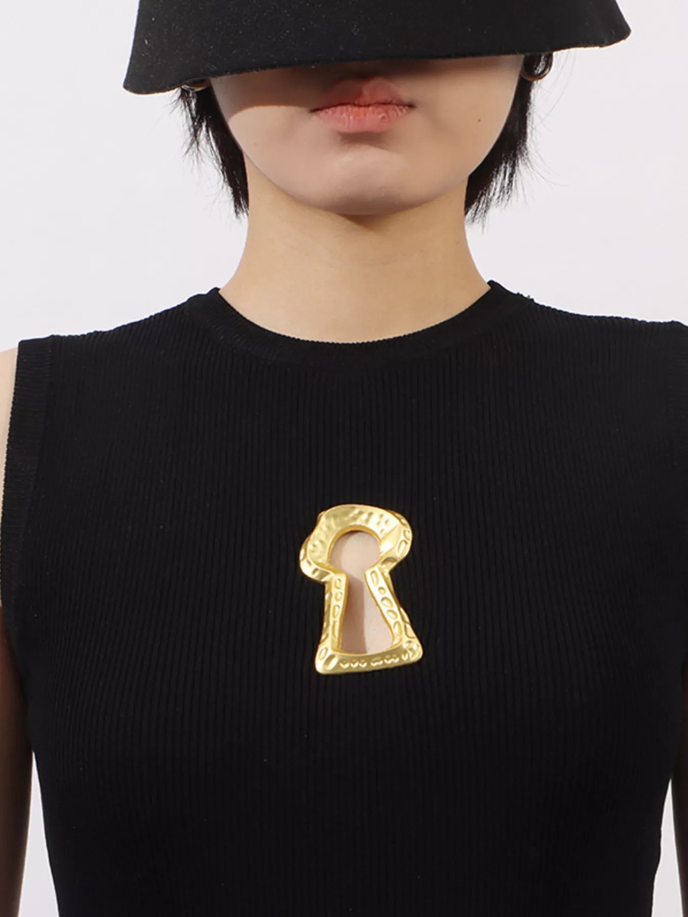NEWYORKLISTED RUNWAY STYLE: Person wearing a black sleeveless top with a gold keyhole brooch on a white background