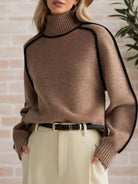 Person wearing a brown sweater with black accents against a light brick wall.