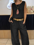 NEWYORKLISTED COMFORT COLLECTION: Person wearing a black sleeveless top and wide-leg pants with a belt, standing indoors.