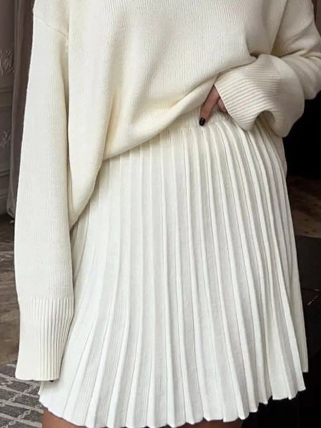 NEWYORKLISTED STYLE COLLECTION: Person wearing a cream sweater and pleated white skirt.