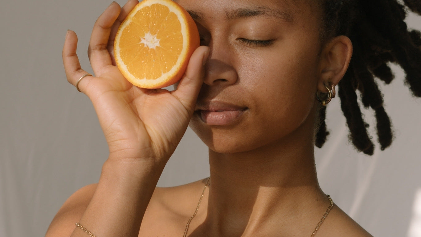 NEWYORKLISTED COSMETIC COLLECTION: Grow Hair Oil, Woman holding a sliced orange to her face against a neutral background