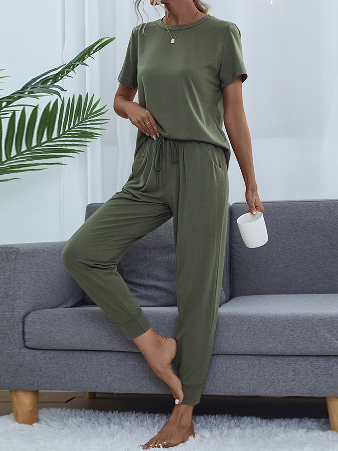 NEWYORKLISTED Intimate Apparel: Person wearing an olive green outfit sitting on a gray sofa with a plant in the background