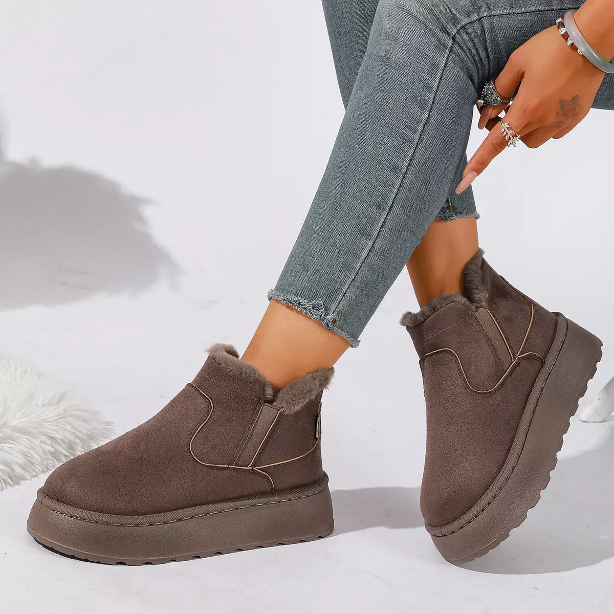 NEWYORKLISTED SHOE COLLECTION: A person wearing taupe-brown platform Chelsea-style ankle boots with fuzzy shearling lining, paired with gray skinny jeans, shown against a white studio background.