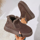 NEWYORKLISTED SHOE COLLECTION: A pair of women's mid-calf winter boots in dark brown suede with plush faux-fur lining, shown being worn with one boot raised and the other held by a hand. The boots feature elastic side panels and a thick lug sole.