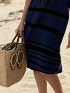 NEWYORKLISTED STYLE COLLECTION: Person wearing a blue and black striped dress holding a straw bag on a beach.